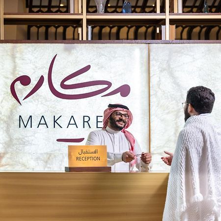 마카렘 아지아드 마카 호텔 메카 외부 사진 The photo depicts a reception area in a hotel or establishment named "Makarem." In the image, a receptionist, dressed in traditional attire, is smiling and interacting with a guest who is wearing a white robe, commonly known as a thobe or ihram. The 