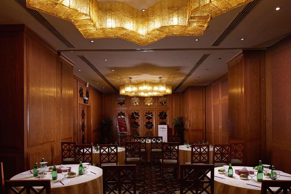 마카렘 아지아드 마카 호텔 메카 시설 사진 The photo shows a well-decorated dining room with wooden paneling and elegant furnishings. There are round tables covered with tablecloths, and each table is arranged with glasses of water. The lighting is warm, provided by elaborate chandeliers on t