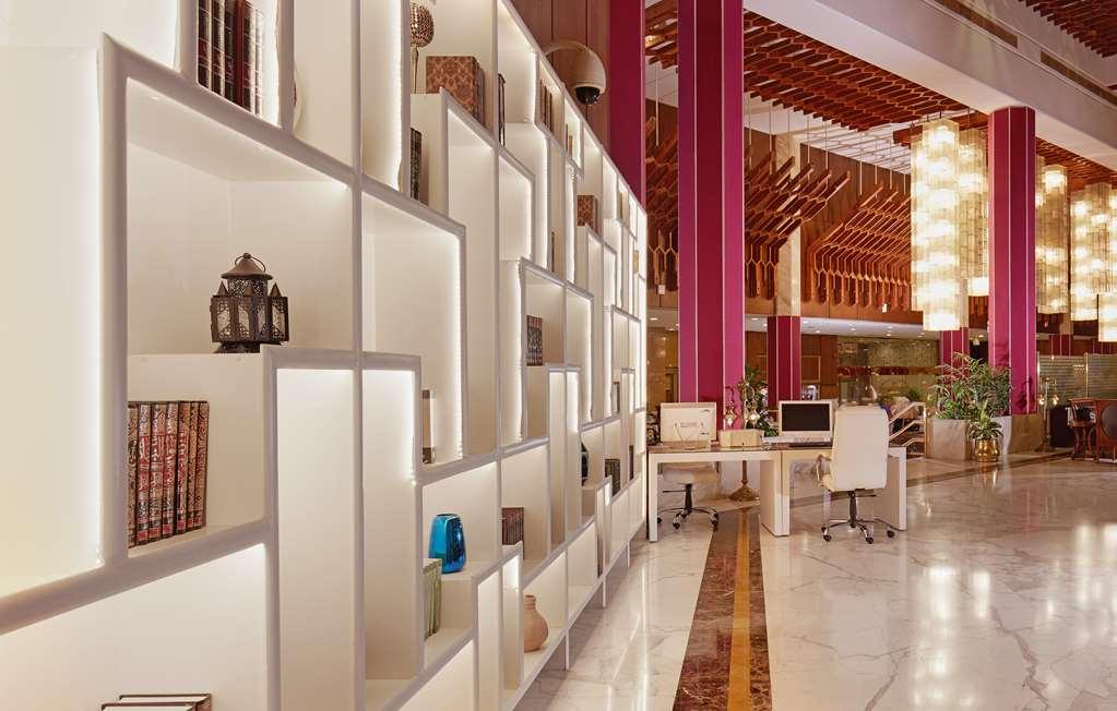 마카렘 아지아드 마카 호텔 메카 내부 사진 The photo shows a modern interior space, likely a lobby or lounge area of a stylish hotel or building. There is a partition wall made up of white shelving units illuminated from within, displaying various decorative items, books, and vases. The desig