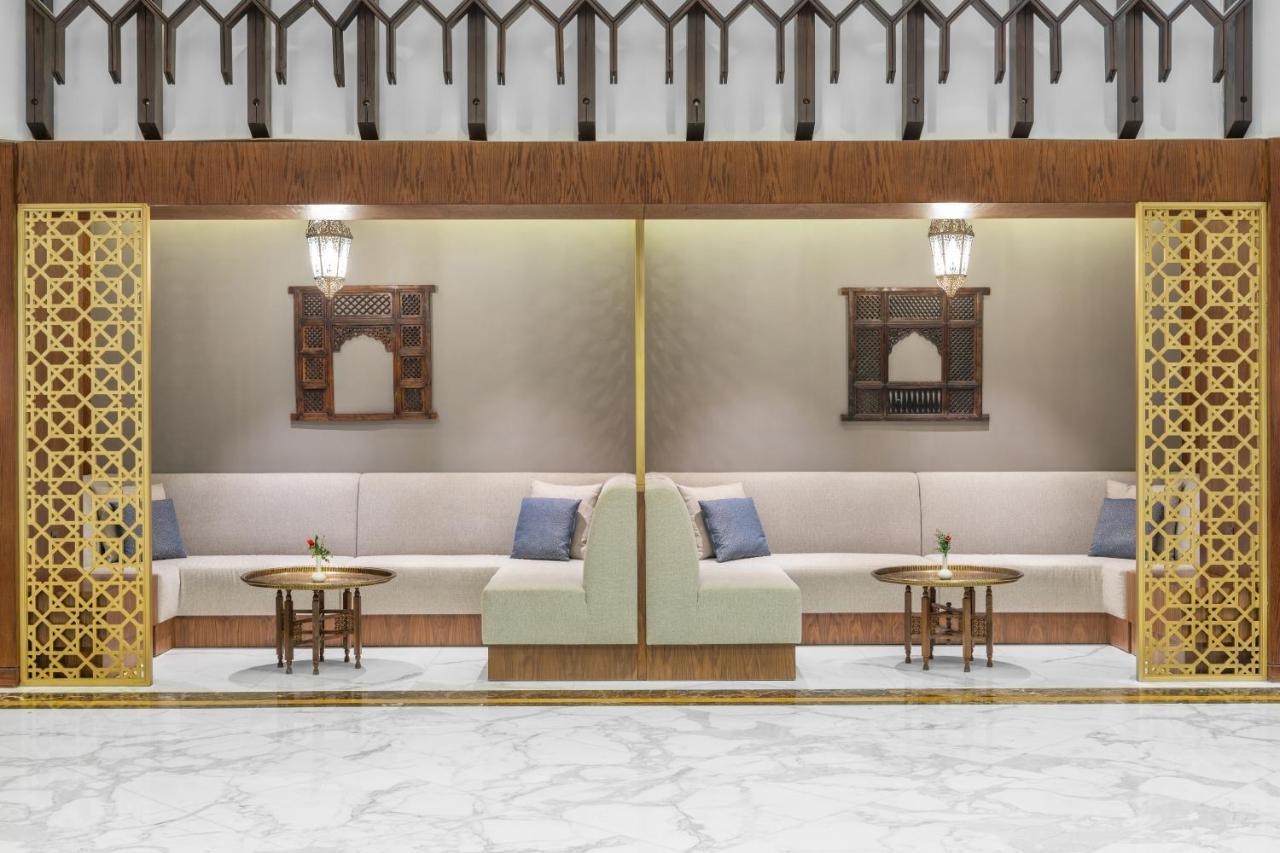 마카렘 아지아드 마카 호텔 메카 외부 사진 The photo depicts a modern, elegantly designed seating area. It features a pair of sofas with light-colored upholstery, accented by blue cushions. There are several small tables in front of the sofas, likely meant for drinks or decorative items. The 