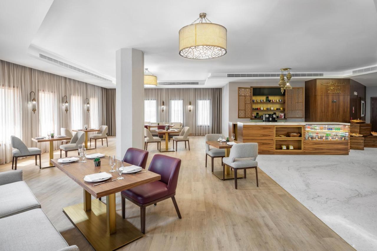 마카렘 아지아드 마카 호텔 메카 외부 사진 The photo depicts a modern and stylish restaurant interior. The space features a combination of wooden and upholstered furniture, with several dining tables arranged throughout. The tables are set with dishes and cutlery, indicating readiness for ser