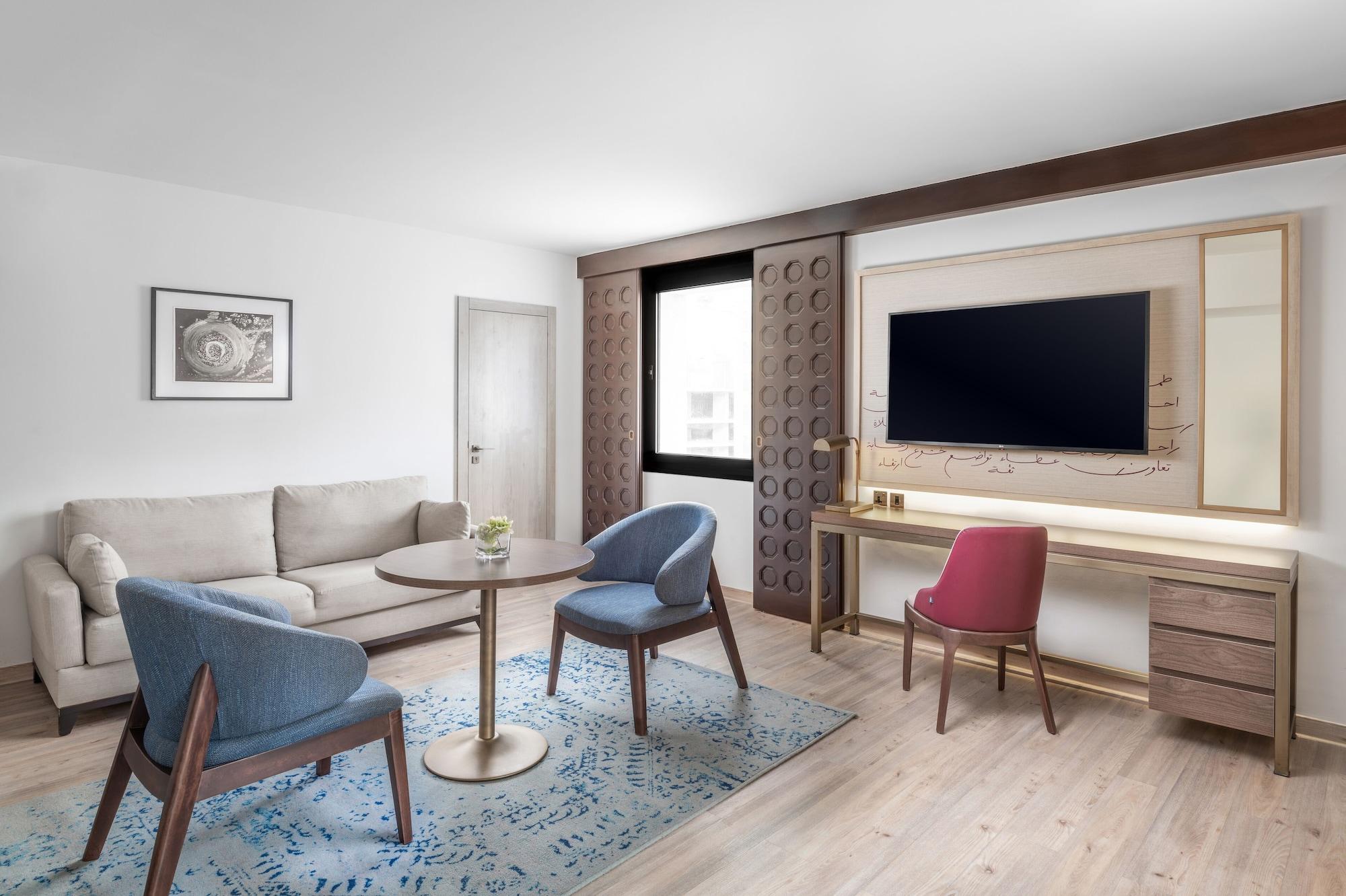 마카렘 아지아드 마카 호텔 메카 외부 사진 The photo shows a modern living room setting. It features a light-colored sofa positioned against one wall, accompanied by a round table at the center. Two stylish chairs, one in blue and the other in pink, are placed around the table. There is a lar