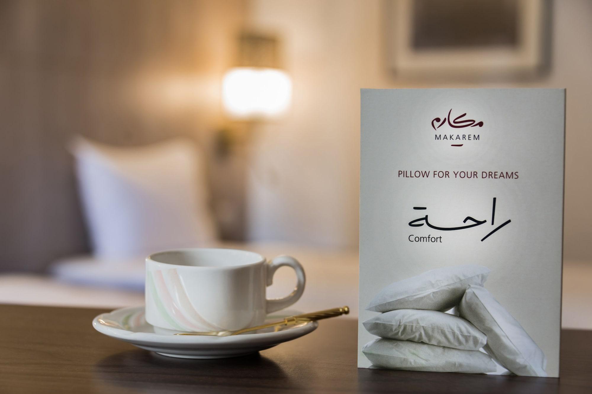 마카렘 아지아드 마카 호텔 메카 외부 사진 The image features a cozy setting, likely a hotel room. In the foreground, there is a white cup of coffee or tea placed on a small saucer, accompanied by a gold spoon. Beside the cup is a decorative card or sign that reads "Pillow for Your Dreams" an