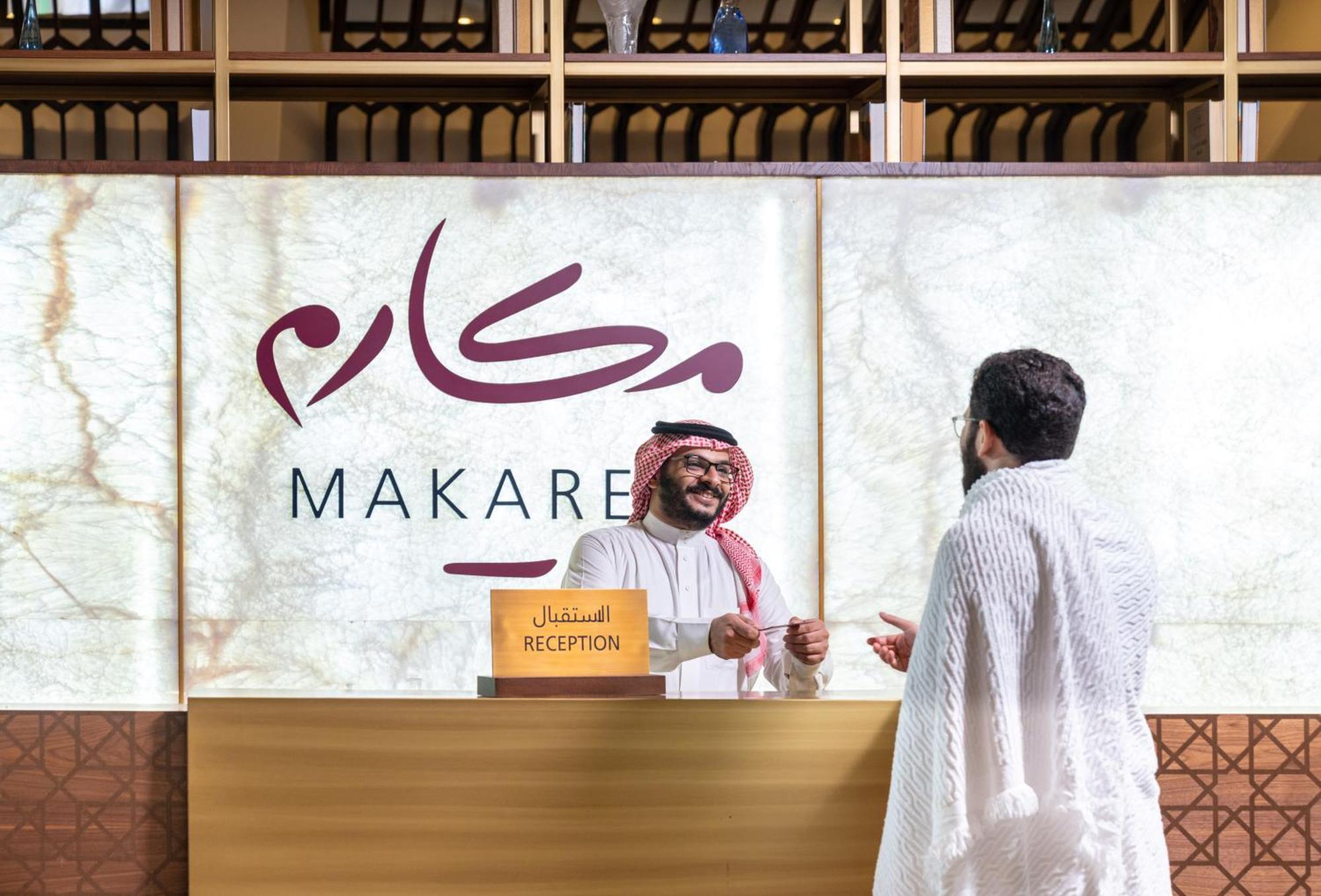마카렘 아지아드 마카 호텔 메카 외부 사진 The photo depicts a reception area in a hotel or establishment named "Makarem." In the image, a receptionist, dressed in traditional attire, is smiling and interacting with a guest who is wearing a white robe, commonly known as a thobe or ihram. The 