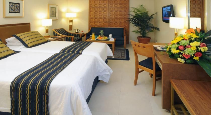 마카렘 아지아드 마카 호텔 메카 외부 사진 The image shows a hotel room featuring two beds with white linens and a decorative stripe along the edge. There is a seating area with two chairs and a small table, set with a breakfast spread that includes fruit and drinks. A small potted plant adds