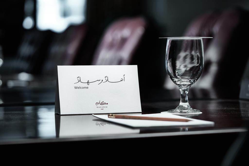 마카렘 아지아드 마카 호텔 메카 외부 사진 The photo depicts a well-arranged table setting. There is a card in both Arabic and English that says "Welcome," placed on the table. Next to the card, there is a clear glass and a pen resting on a piece of paper. The background features leather seat